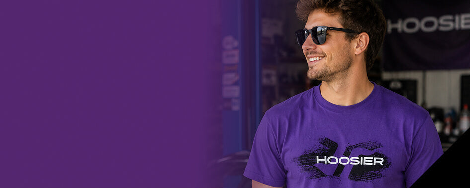 A man wearing a purple Hoosier t-shirt and black sunglasses, standing in front of a dark background with a purple graphic overlay on the left.